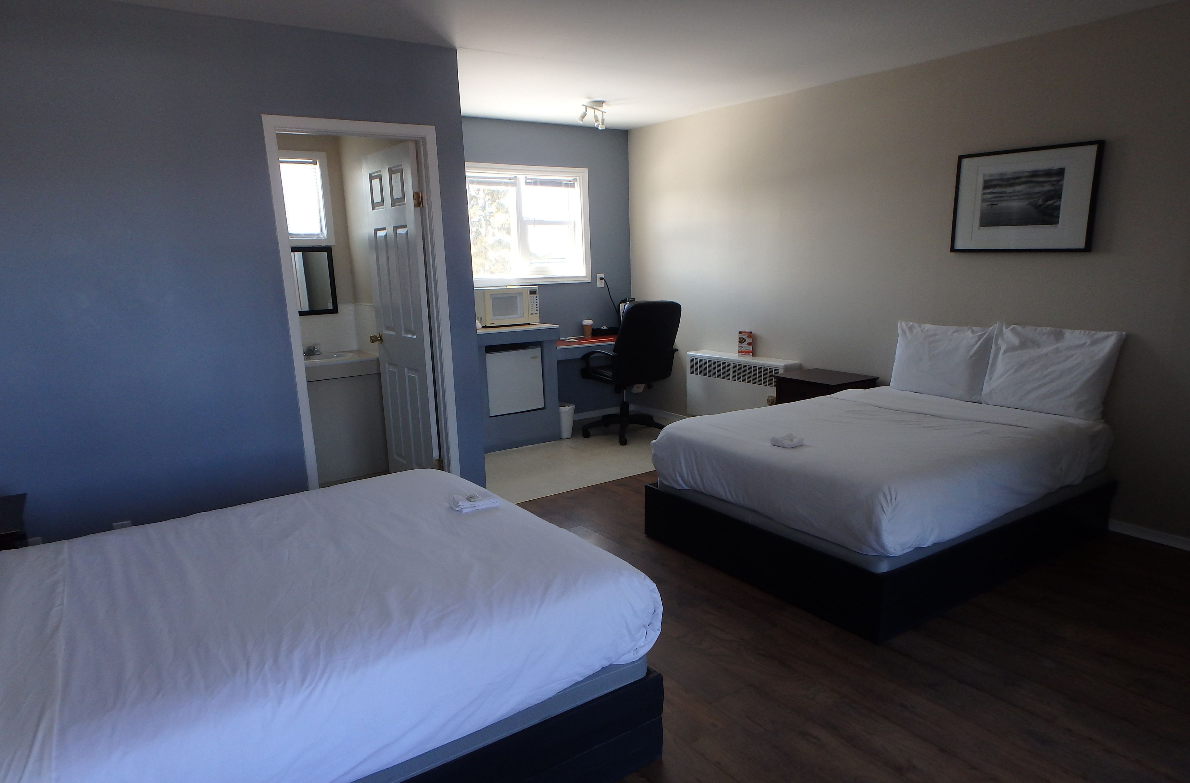A bedroom with two beds, a desk, and a window.