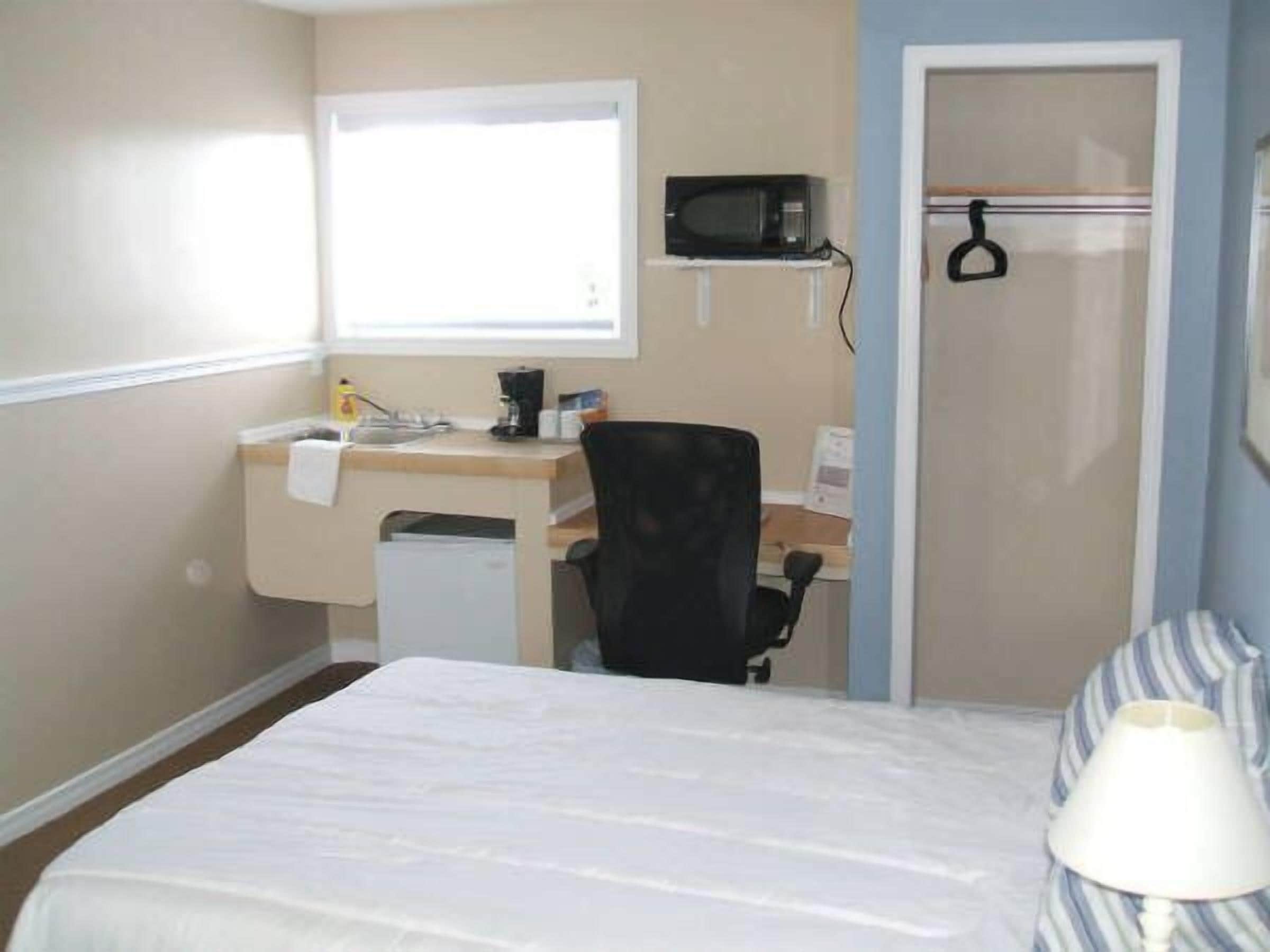 A hotel room with a bed, a desk with a computer, a microwave, and a window.