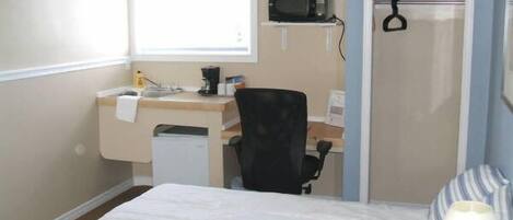 A hotel room with a bed, a desk with a computer, a microwave, and a window.