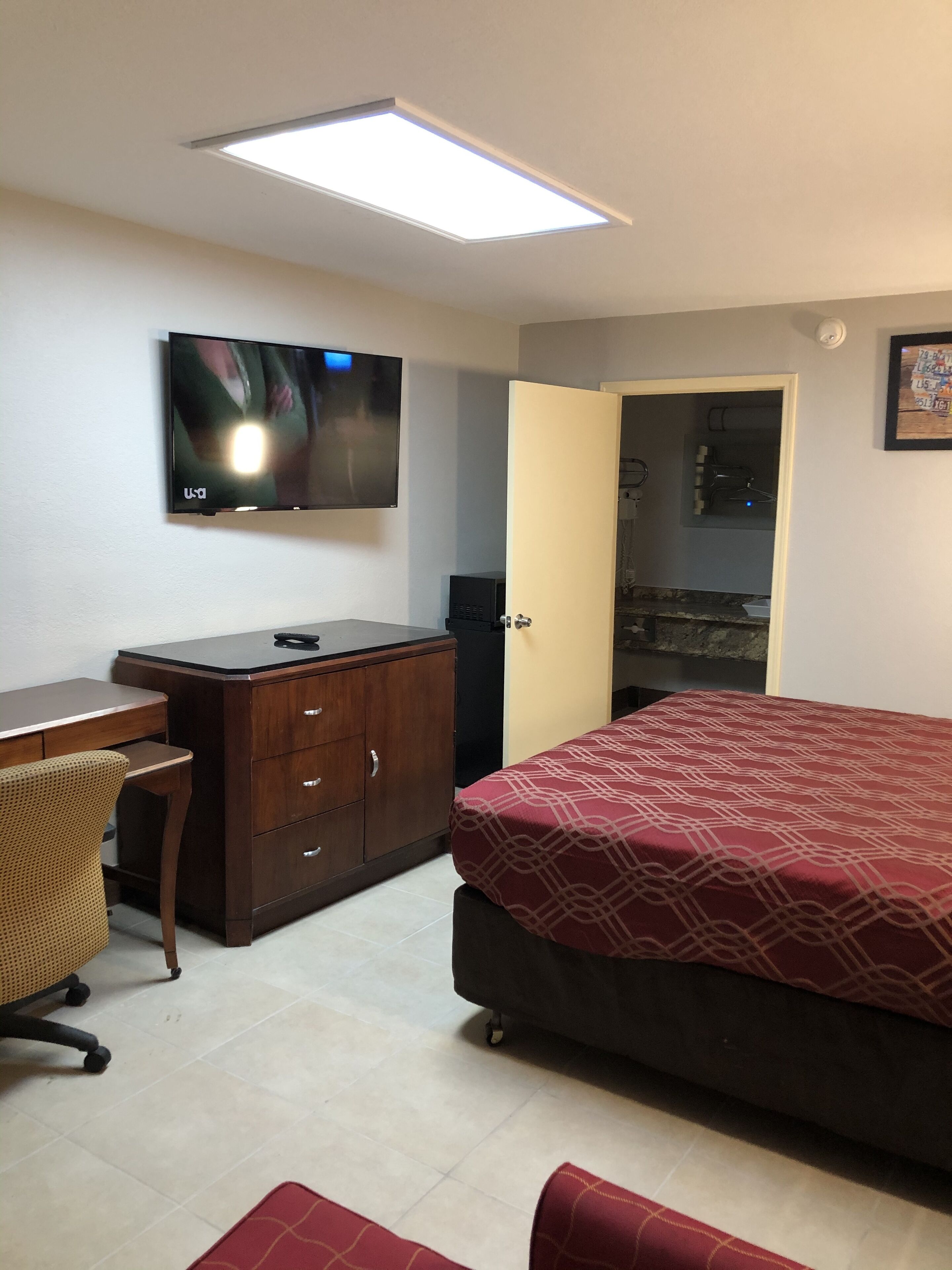 A bedroom with a bed, a desk, a chair, a wardrobe, and a television on the wall.