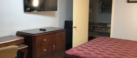 A bedroom with a bed, a desk, a chair, a wardrobe, and a television on the wall.