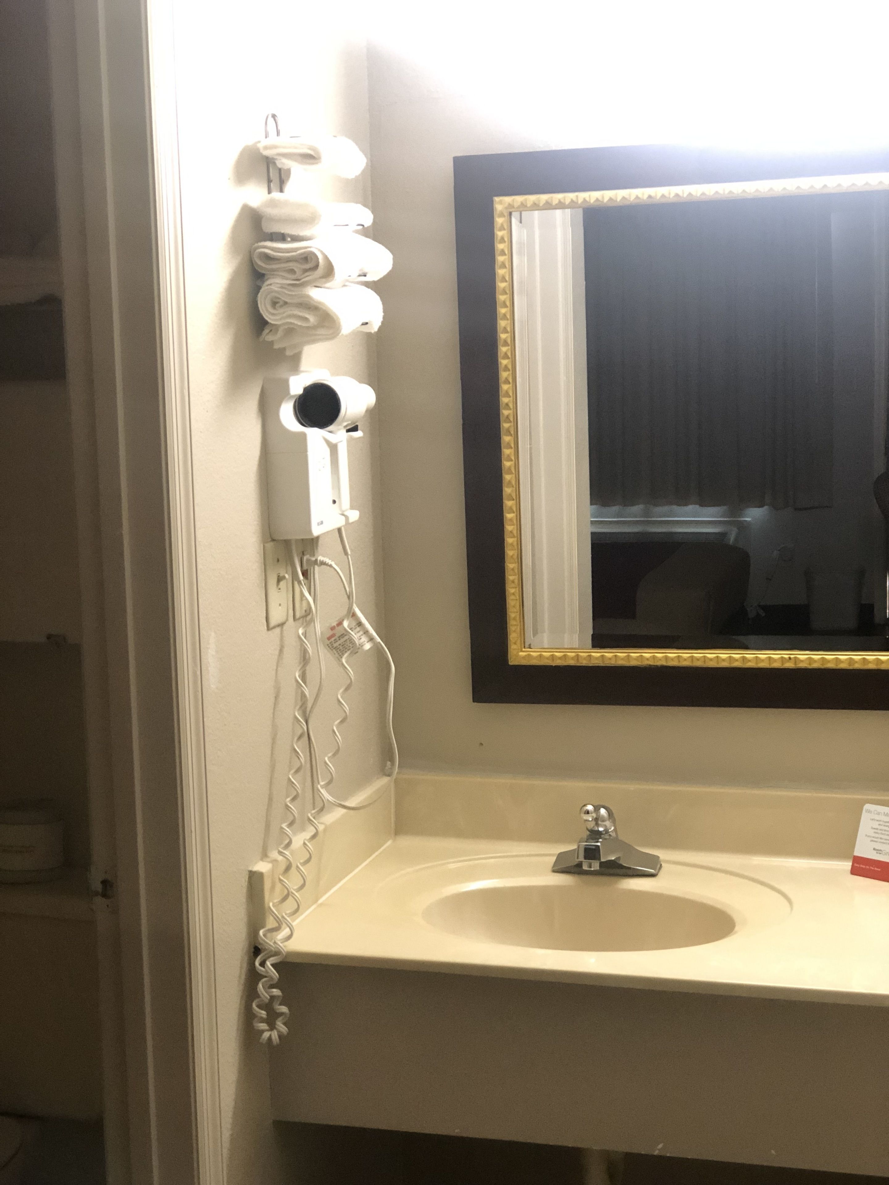 A bathroom with a white sink, a mirror with a gold frame, and a hairdryer mounted on the wall.