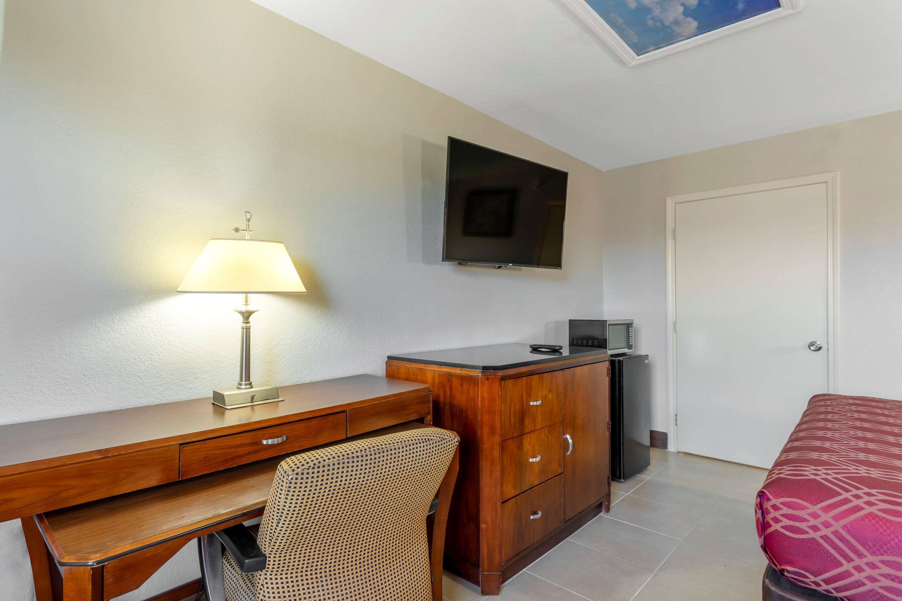 Habitación de hotel con un escritorio de madera, una lámpara, un televisor, una cama y un armario.
