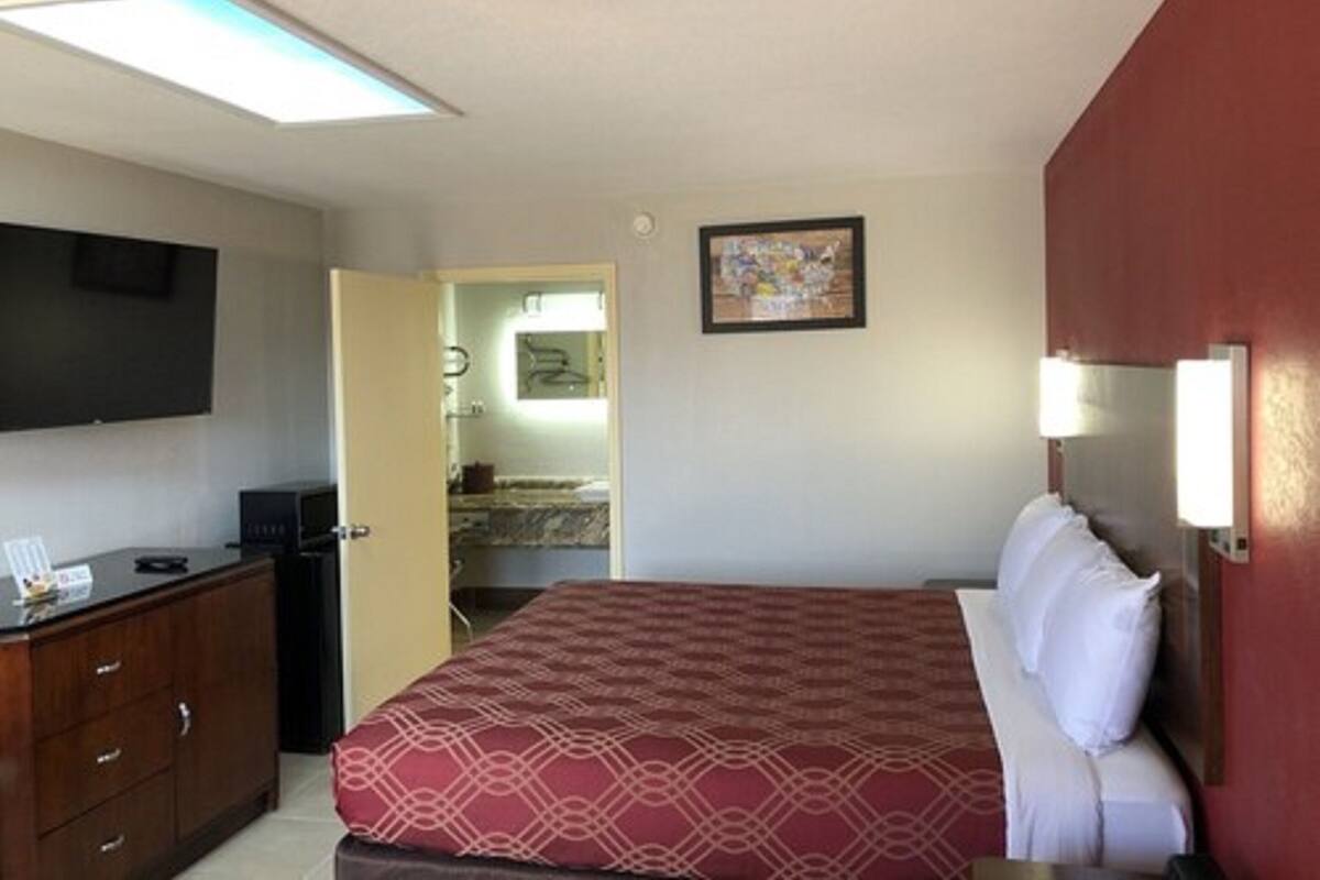 Quarto de hotel com cama, televisão, escrivaninha e banheiro visível por uma porta aberta.