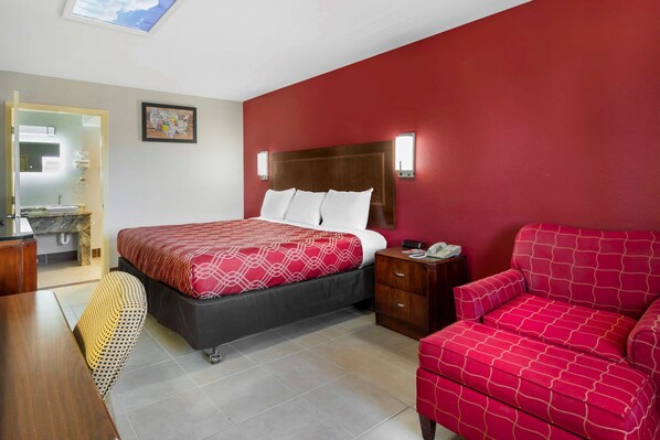 A hotel room with a bed, a nightstand, a red sofa, a chair, and a bathroom visible through an open door. - Econo Lodge Athens I-75 (Athens)