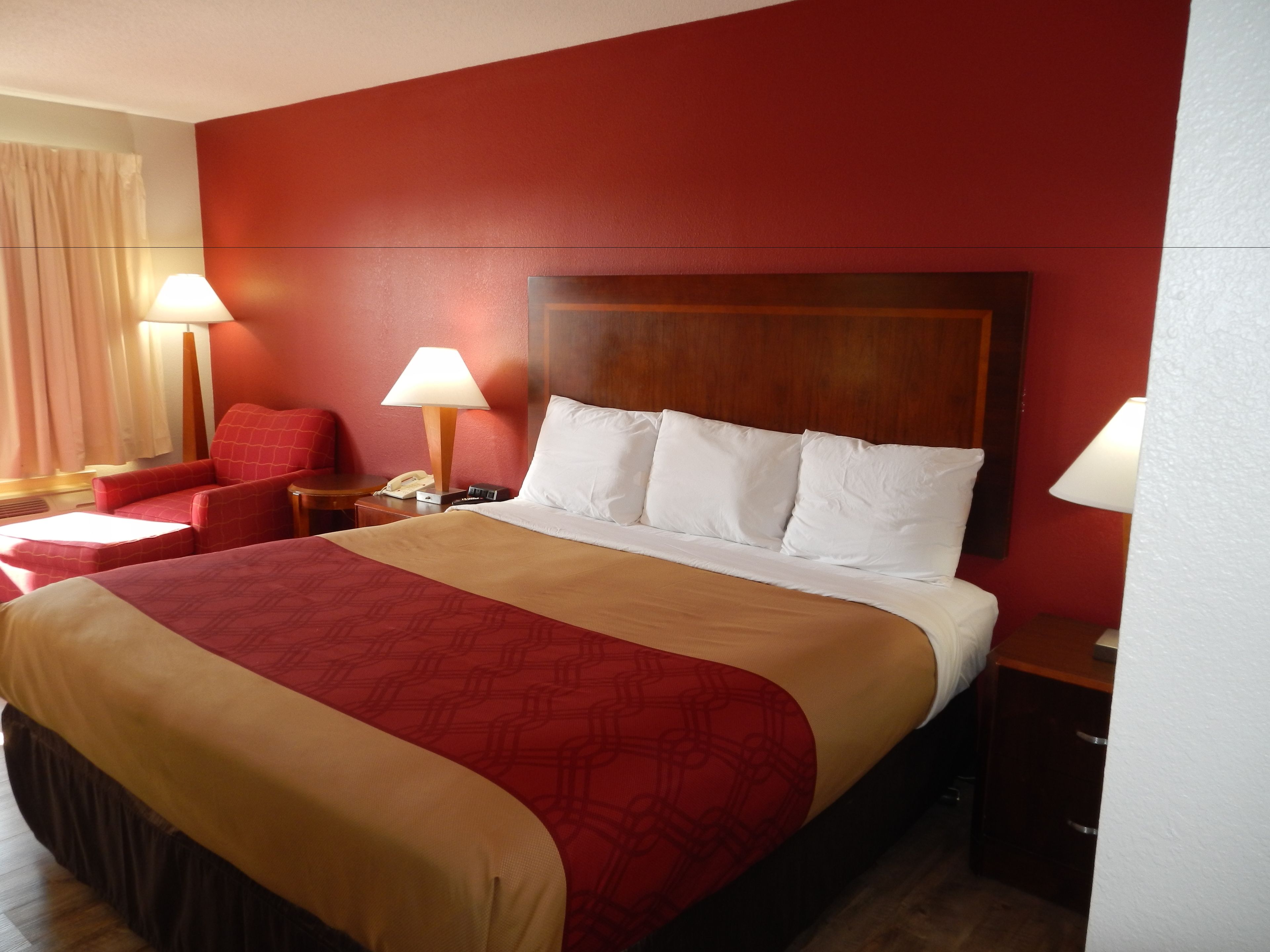 A hotel room with a large bed, two bedside tables, a nightstand, a red armchair, and a lamp.