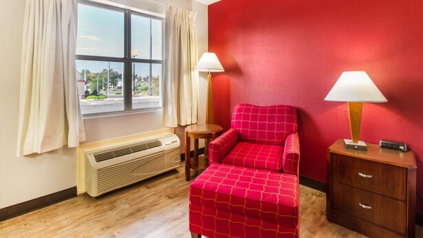 A room with a red wall, a window with curtains, a red sofa, two bedside tables with lamps, and a wooden floor. - Econo Lodge Athens I-75 (Athens)