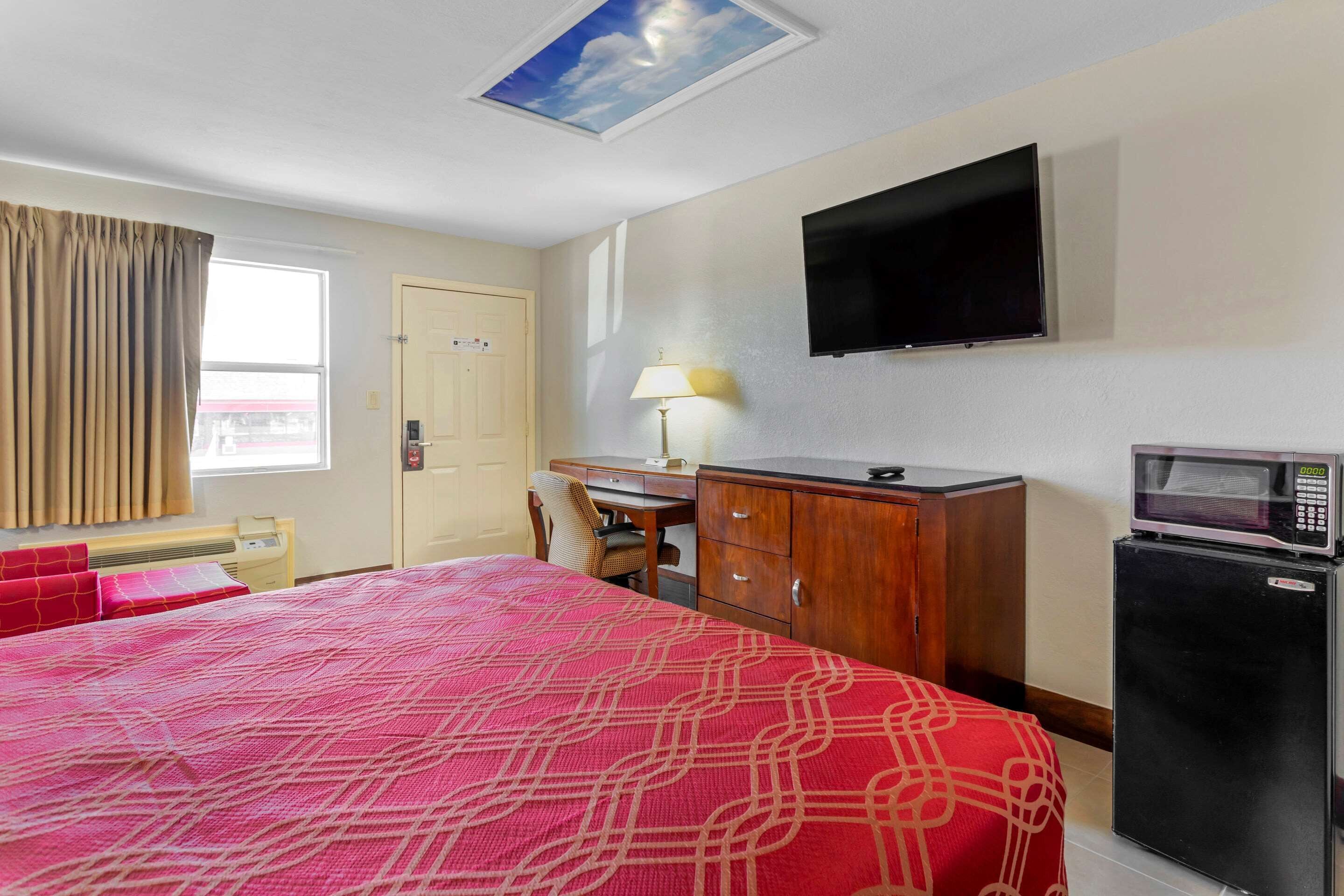 A hotel room with a bed, a desk, a television, a microwave, and a door.