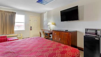 A hotel room with a bed, a desk, a television, a microwave, and a door.