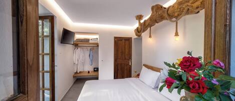 A bedroom with a large bed, a wooden headboard, a wall-mounted TV, and a vase with flowers.