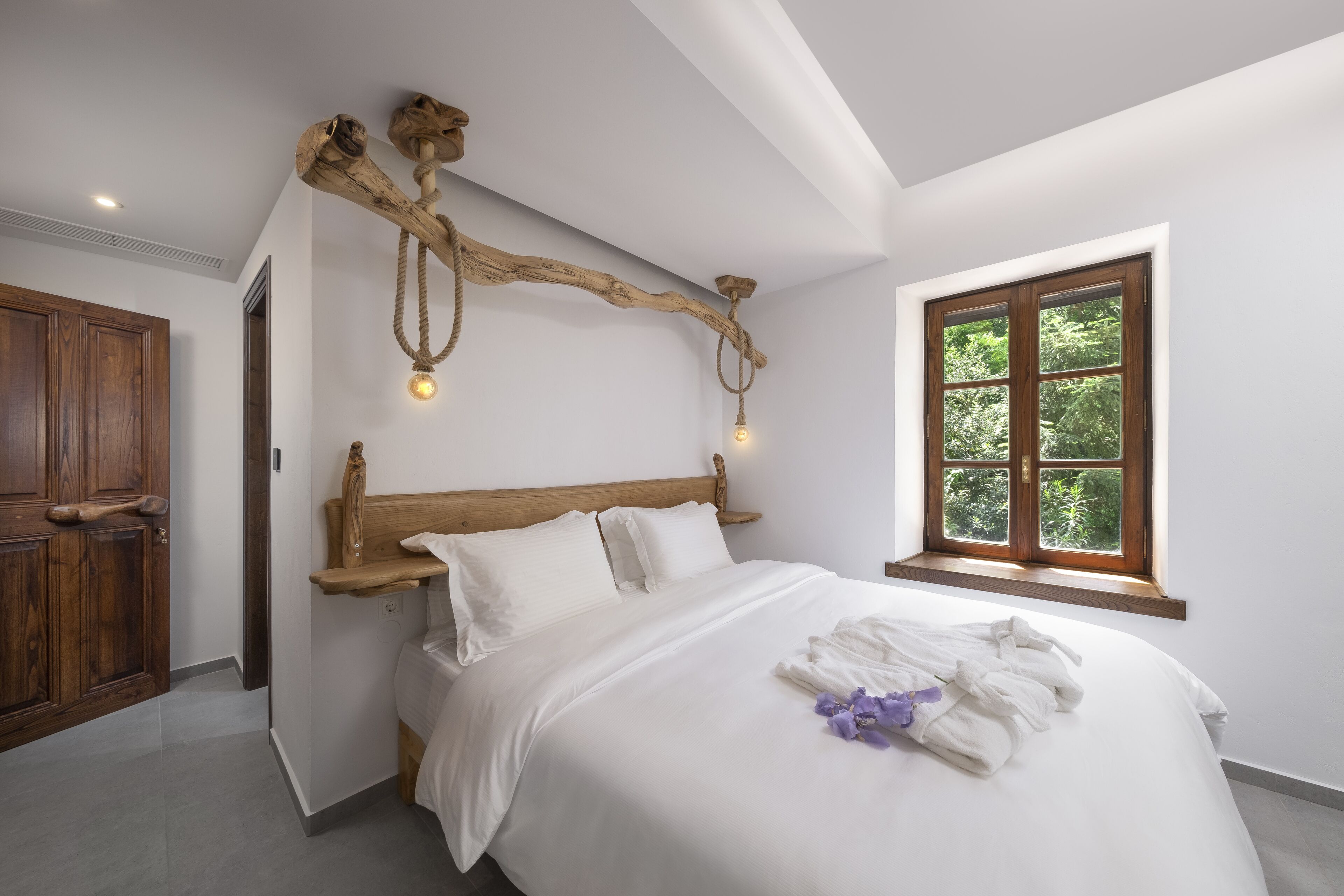 Camera da letto con un letto grande, testiera in legno, una finestra vista su spazi verdi e un lampadario particolare.