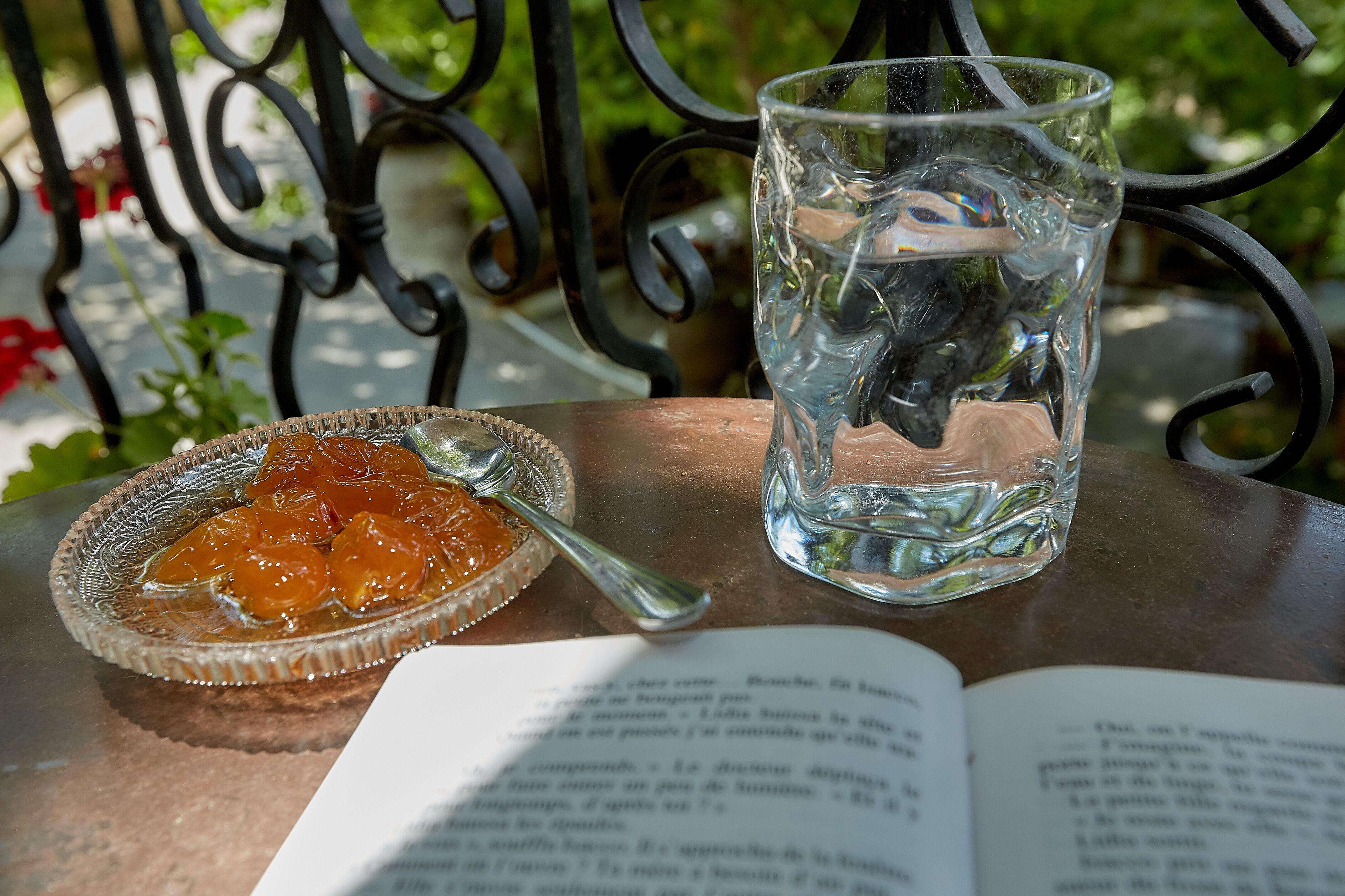 A glass of water, a spoon, and a bowl of fruit on a table with an open book.