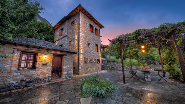 A stone building with a tower, a stone patio, and a pergola with lights. - Palios Stathmos (South Pelion)