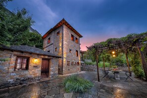 A stone building with a tower, a stone patio, and a pergola with lights. - Palios Stathmos (South Pelion)