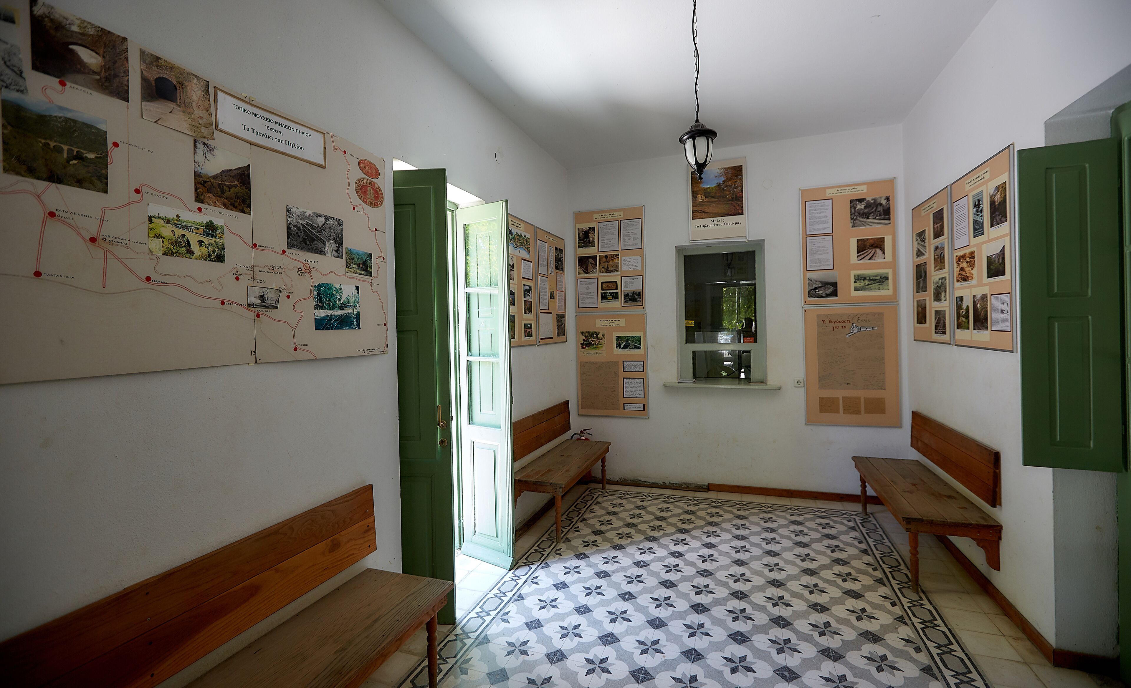A room with a tiled floor, wooden benches, a green door, and walls adorned with informational posters.