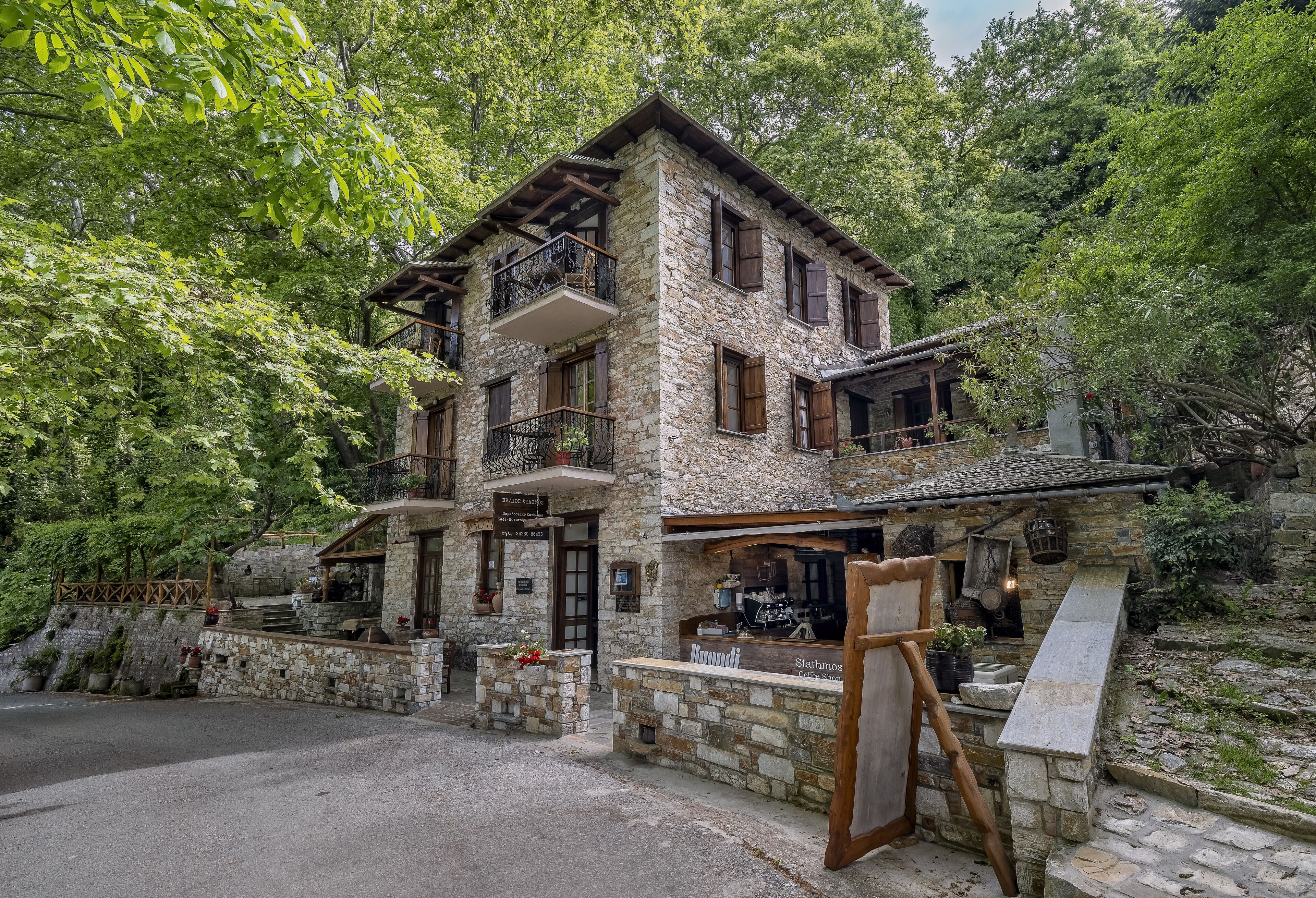 A stone building with a balcony, a wooden staircase, and a sign that reads "Stathmos."