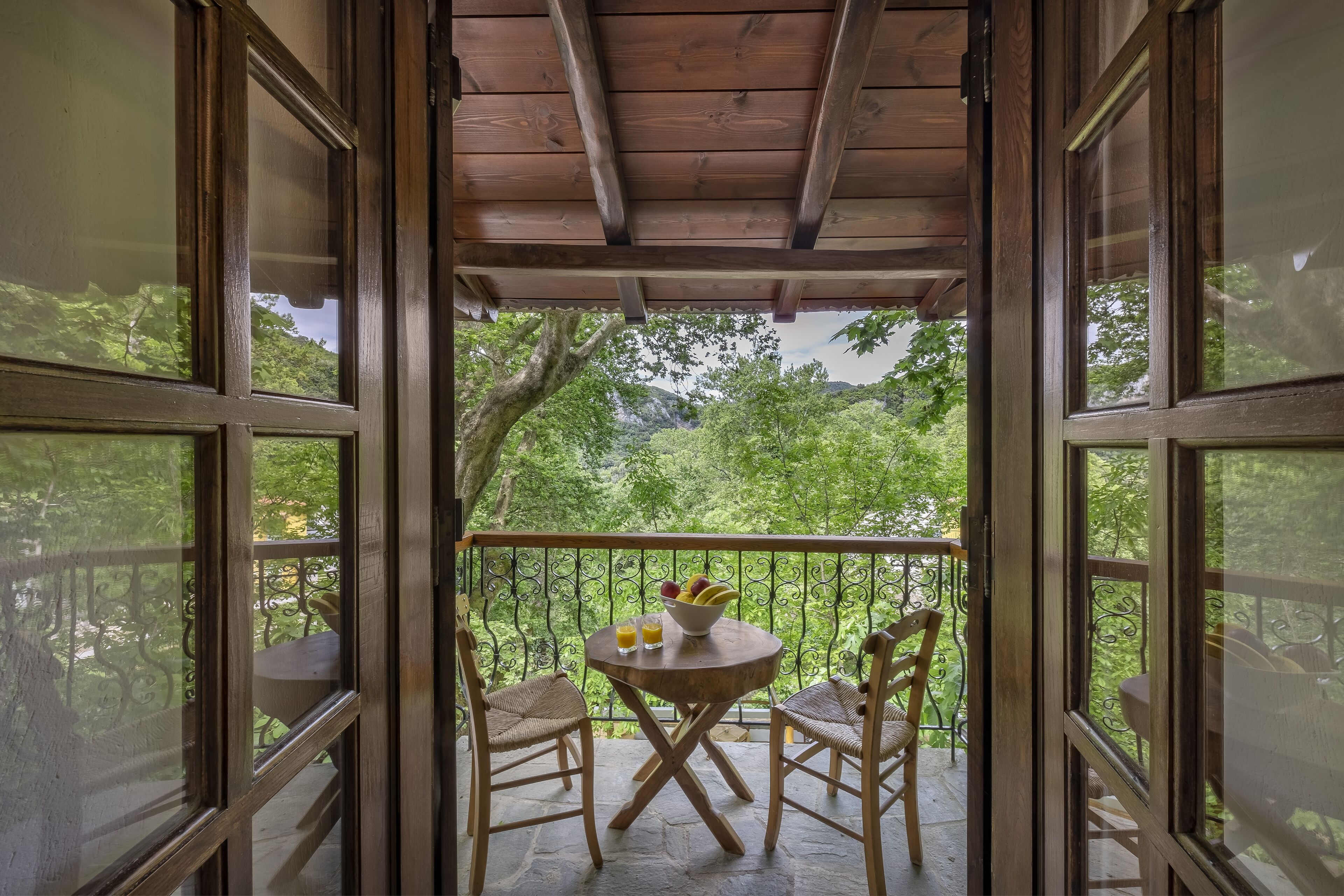 Un balcon en bois avec une table et des chaises, un saladier rempli de fruits et un verre de jus.