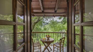 Un balcon en bois avec une table et des chaises, un saladier rempli de fruits et un verre de jus.