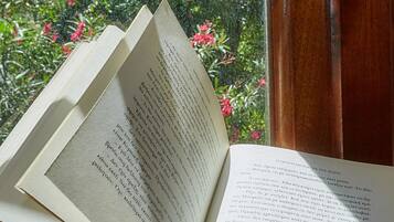 Un livre ouvert sur une surface en bois, près d’une fenêtre donnant sur un paysage verdoyant et fleuri.