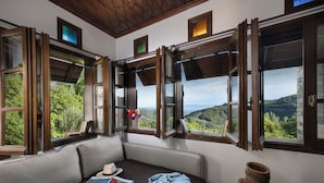 A room with a sofa, open windows, and a view of greenery. - Palios Stathmos (South Pelion)