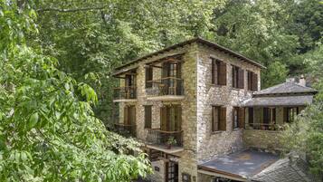 A stone building with multiple balconies, surrounded by lush greenery.