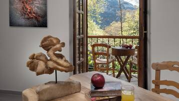 Uma mesa de madeira com um livro, uma maçã e um copo de suco. Há um quadro na parede, e uma TV fixada na parede.