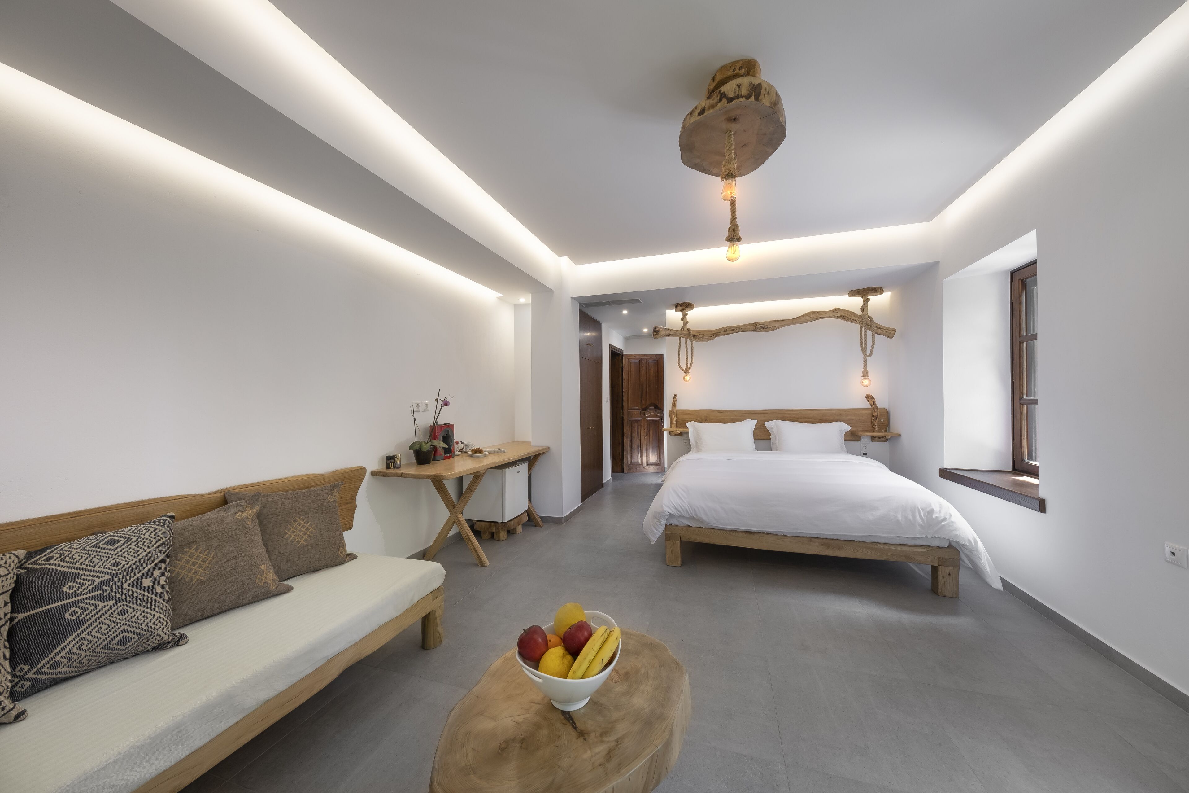 A modern hotel room with a bed, a sofa, a desk, and a fruit bowl.