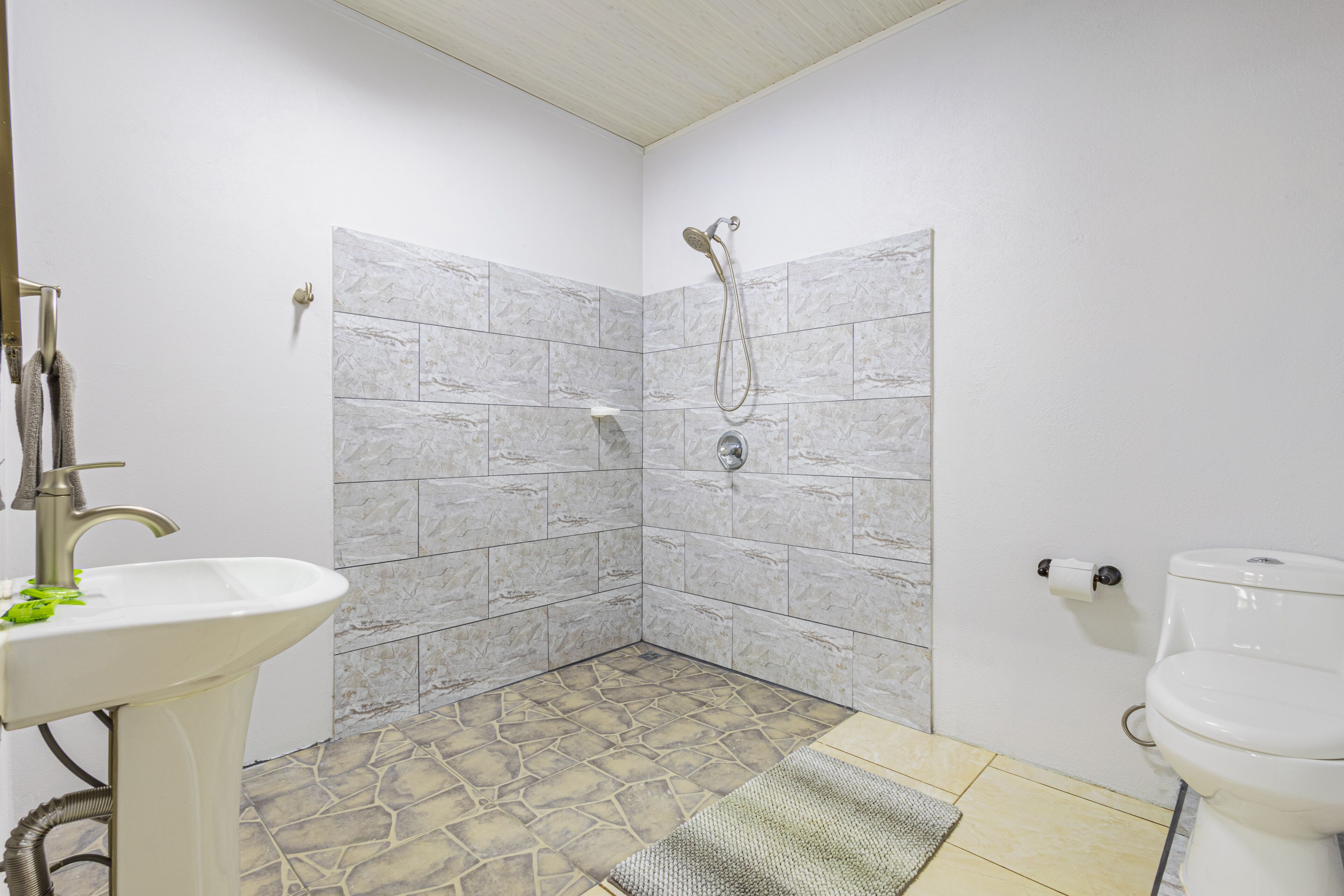 Een badkamer met een douche, wastafel, toilet en betegelde vloer.