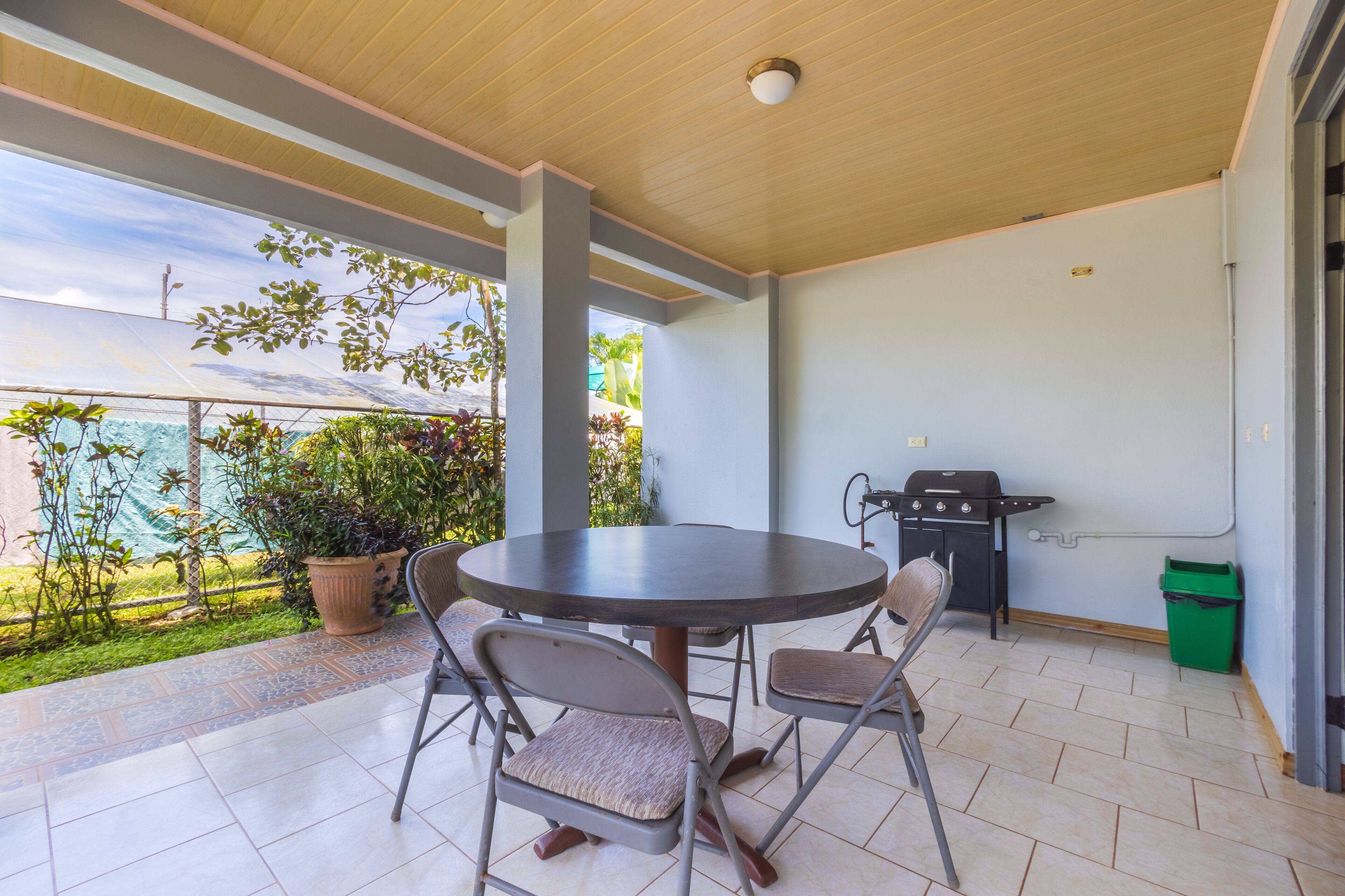 A covered patio with a round table and chairs, a grill, and potted plants.