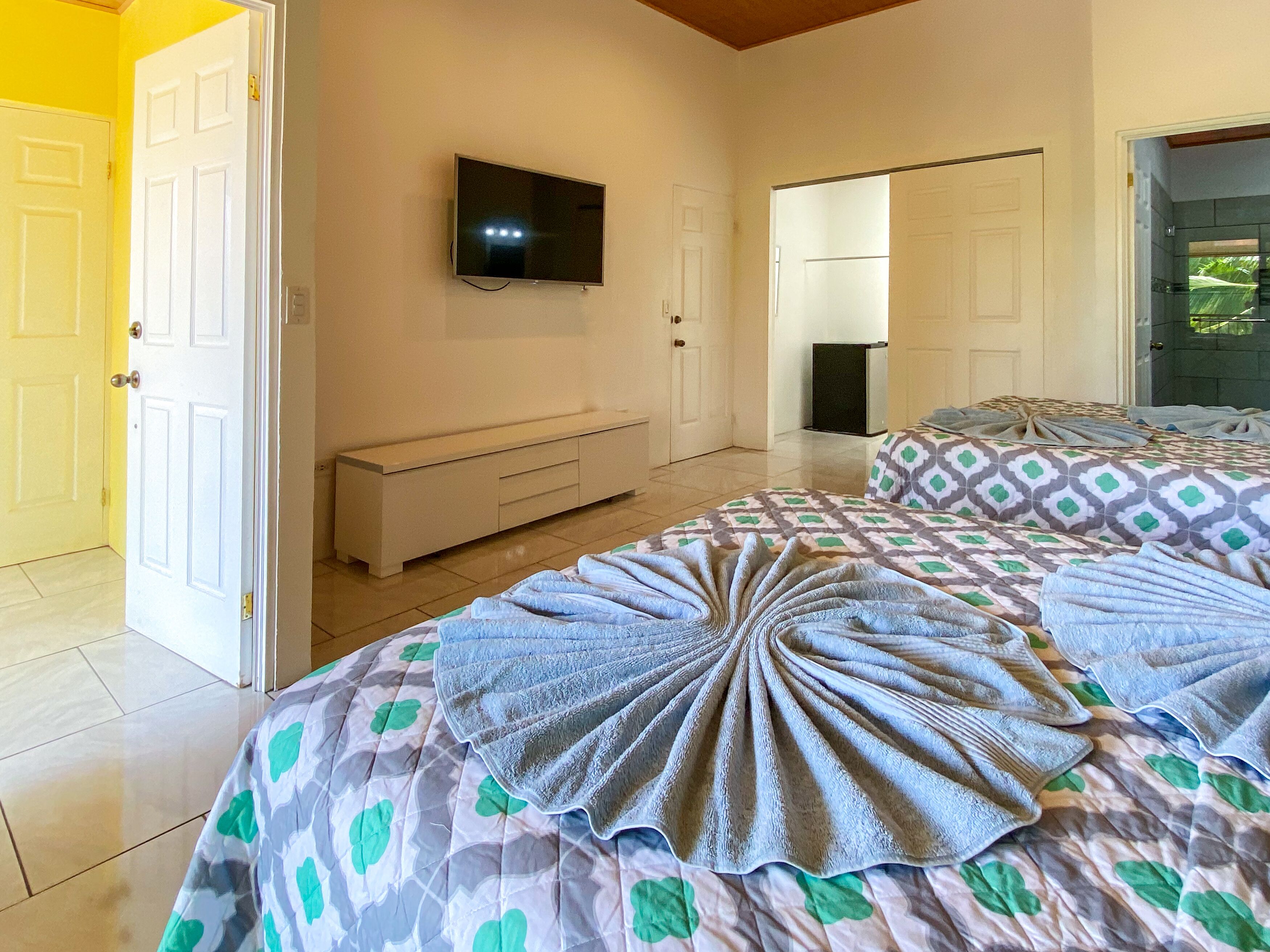 A hotel room with a bed, a TV, a bench, and a door.