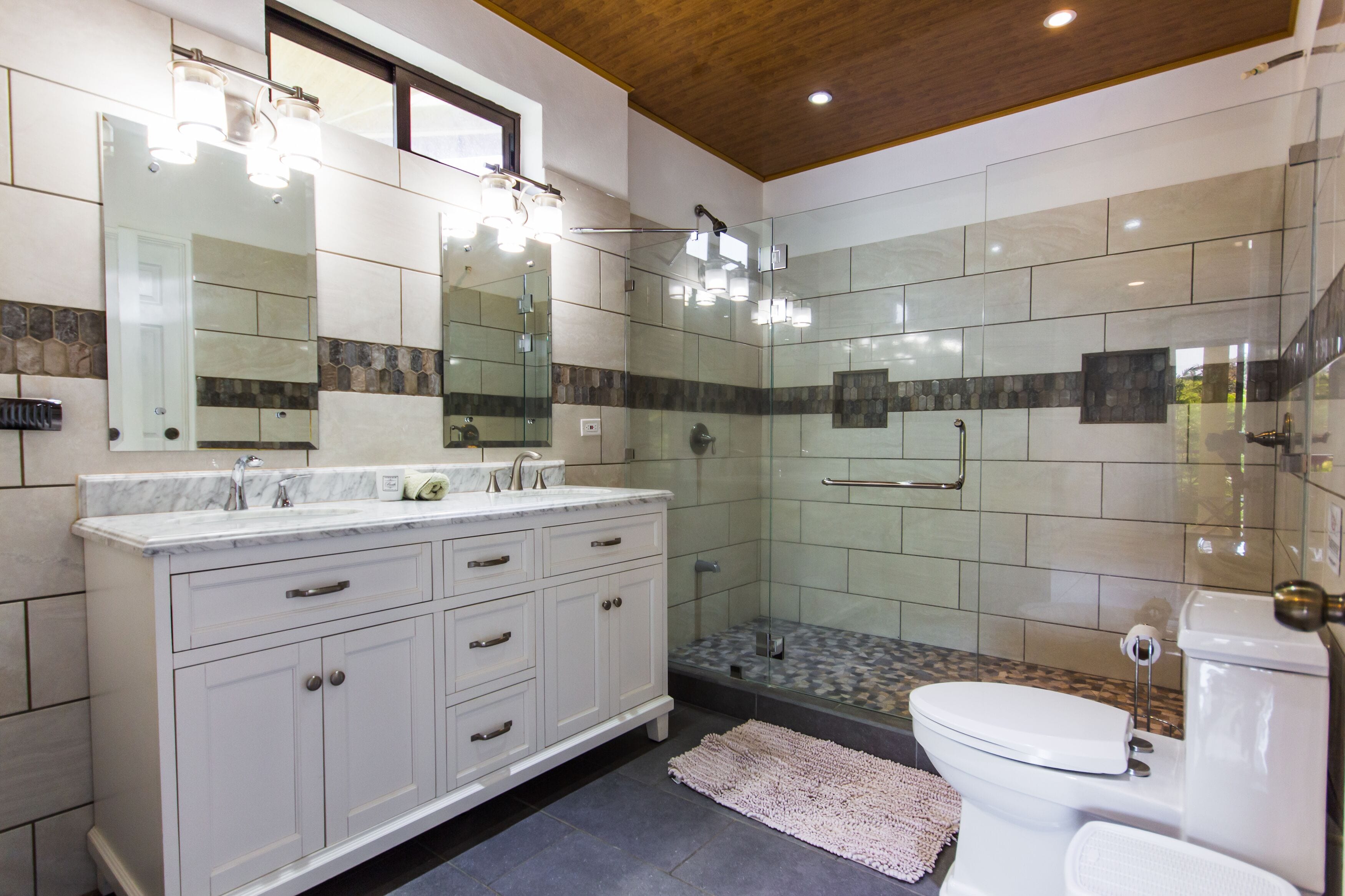 A modern bathroom with a glass-enclosed shower, a white vanity with a marble countertop, and a large mirror above the sink.