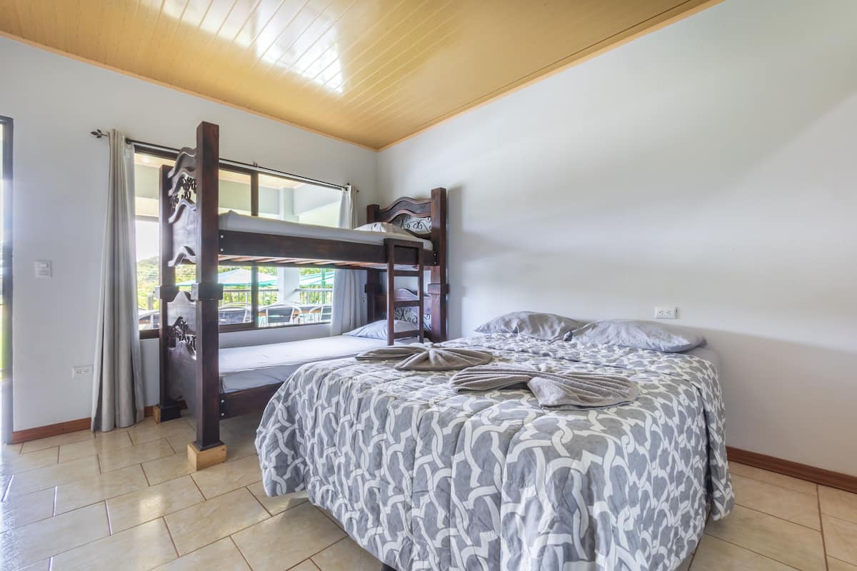 A room with a bunk bed, a window with curtains, and a patterned bedspread.