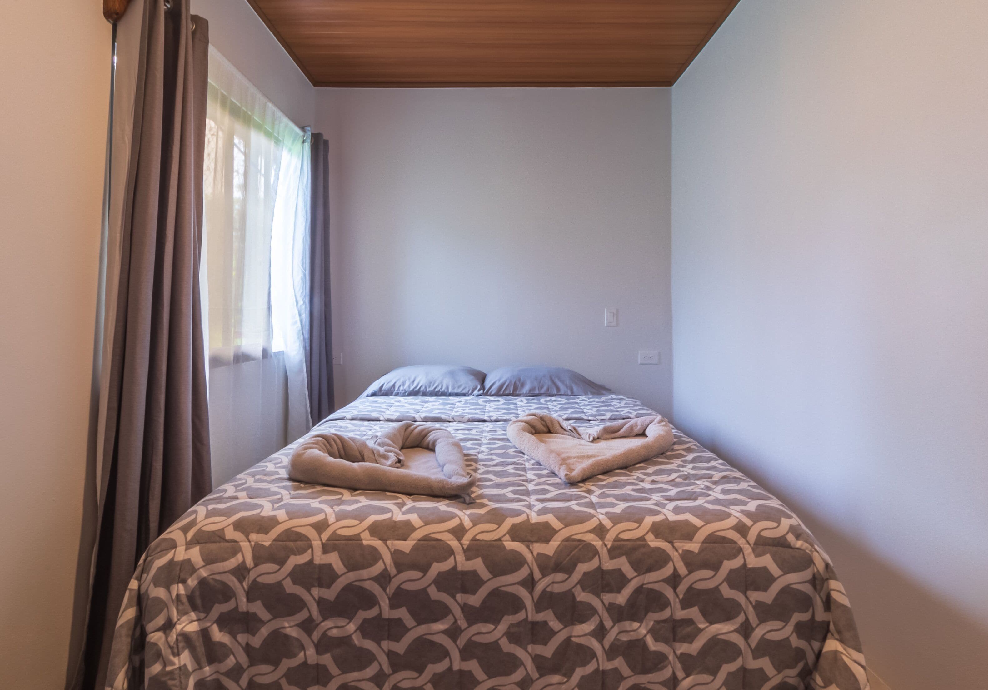 Un dormitorio con cama, cortinas y techo de madera.