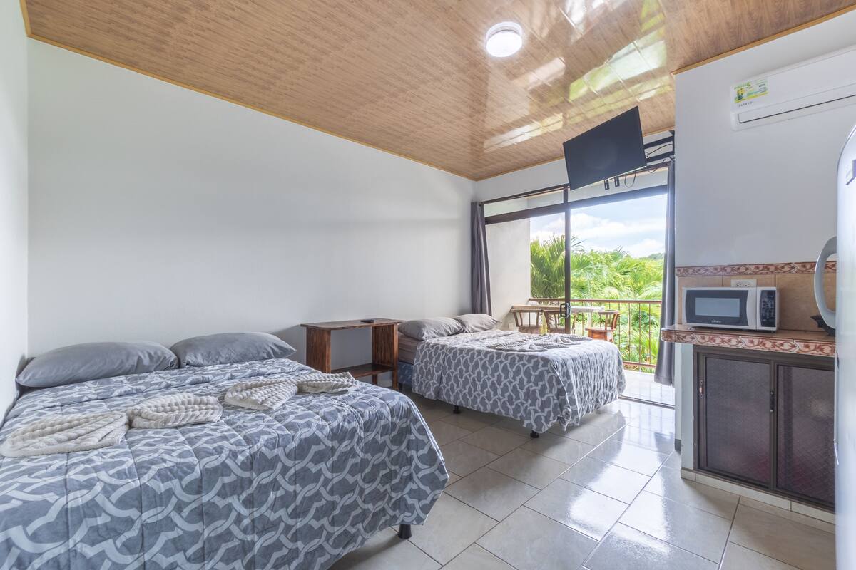 A room with two beds, a small table, a TV, and a kitchenette.