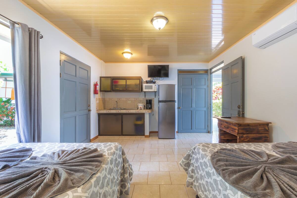 A compact room with two beds, a kitchenette, and a small bathroom.