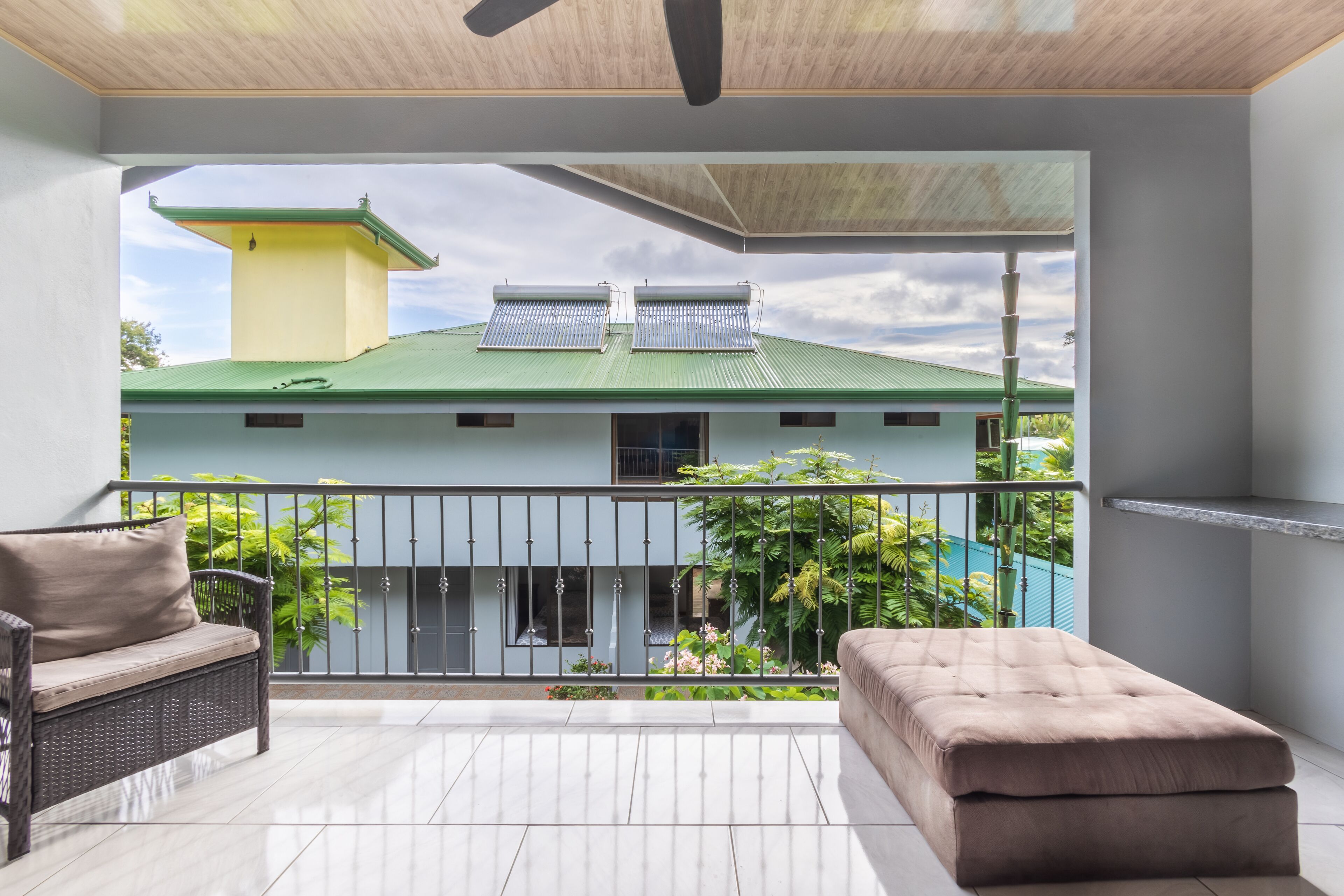 Varanda com sofá, repouso para os pés, ventilador de teto e vista para um edifício com painéis solares.