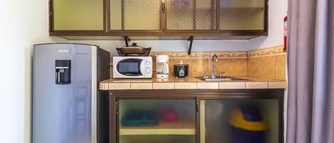 Eine kleine Küche mit Kühlschrank, Mikrowelle, Kaffeemaschine und Spüle.