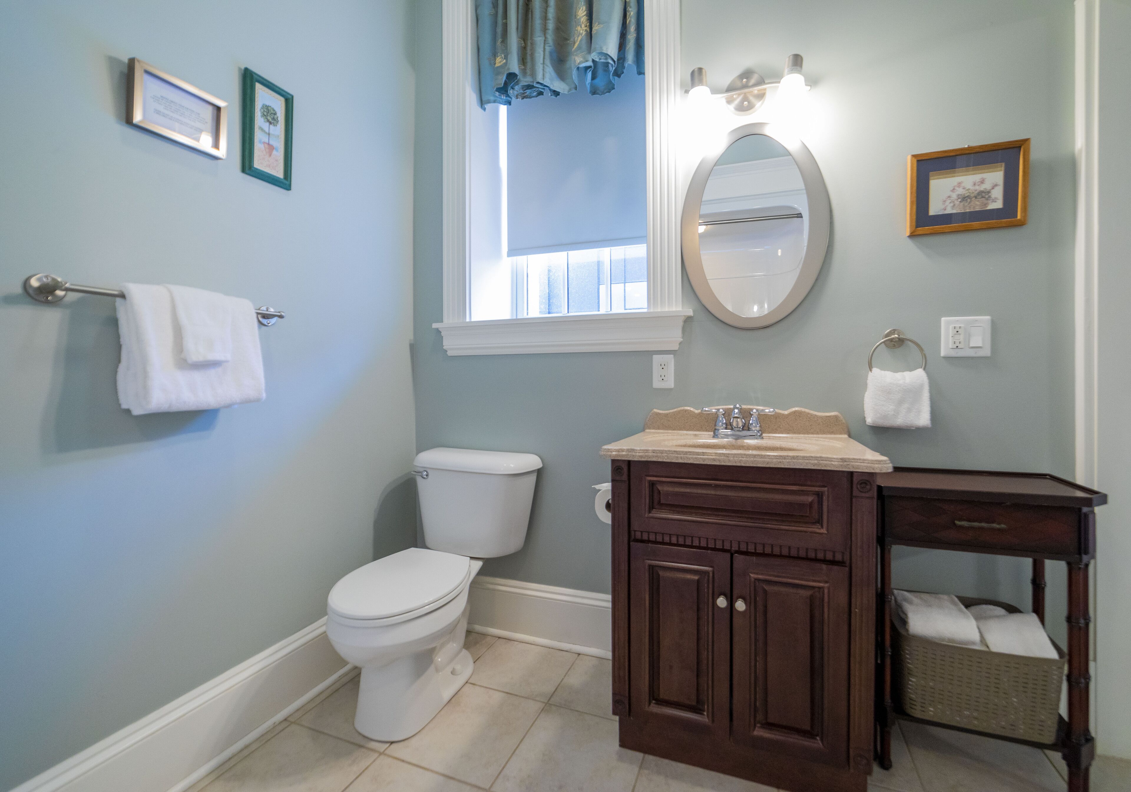 A bathroom with a toilet, vanity, and a window with curtains.