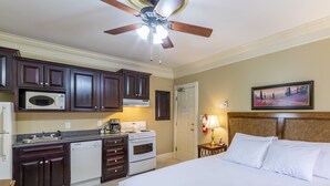 A hotel room with a bed, a desk with a lamp, a microwave, a stove, and a ceiling fan. - Chipman Hill Suites on Union (Saint John)