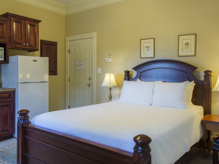 Una habitación de hotel con una cama, lámparas de noche, una silla, un escritorio, un microondas, un refrigerador y armarios de madera.