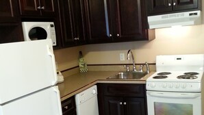 A kitchen with dark wooden cabinets, a white refrigerator, a dishwasher, a sink, and a stove. - Chipman Hill Suites on Union (Saint John)