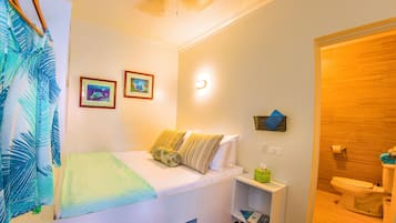 Habitación de hotel con cama, mesita de noche con lámpara, estante en la pared con caja de pañuelos y baño con inodoro y lavamanos.