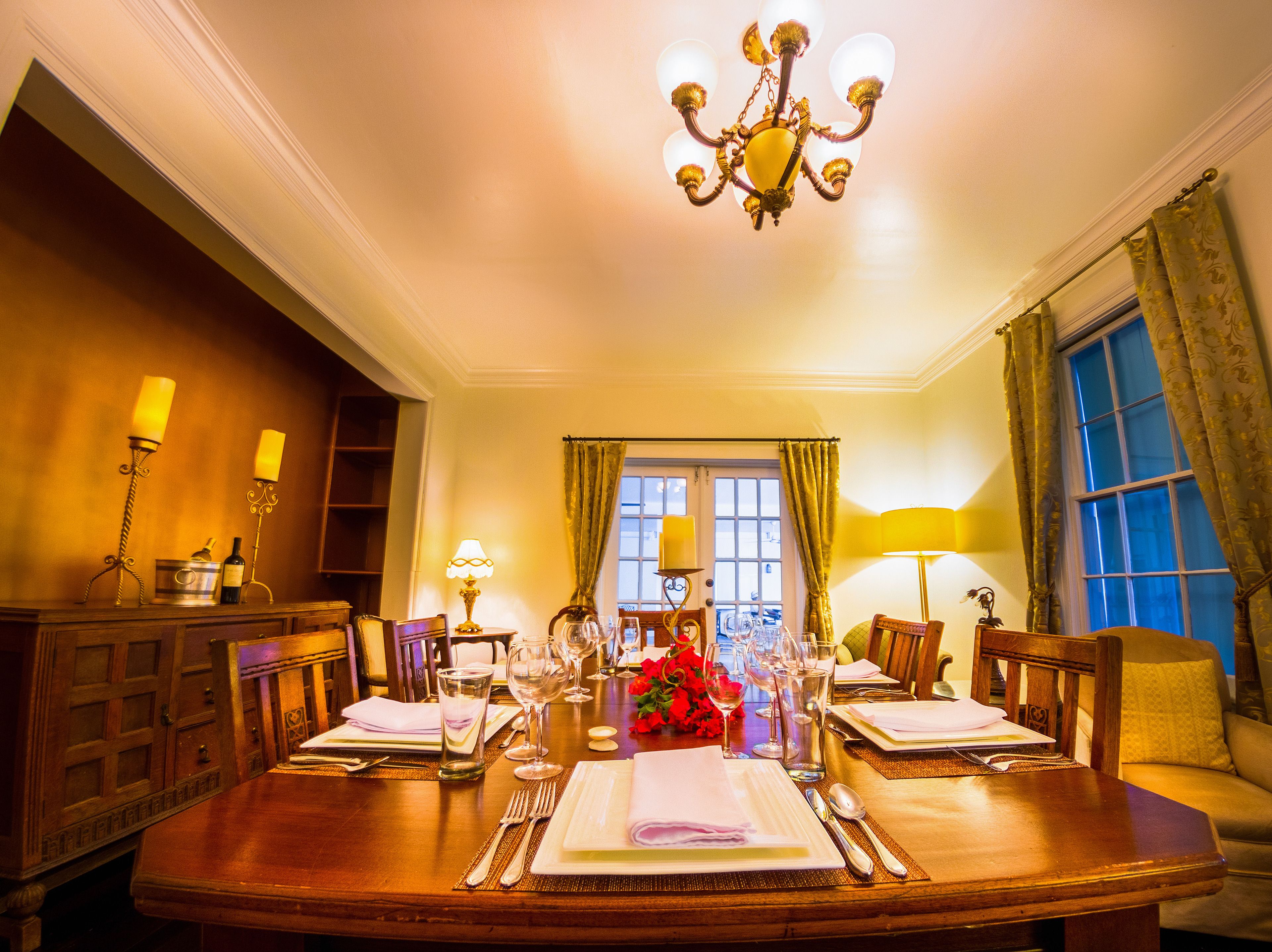 Comedor con una mesa redonda dispuesta para dos personas, un candelabro y una ventana con cortinas.