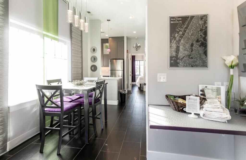 A modern kitchen with dark flooring, a dining area with purple chairs, and a counter with towels and a basket.