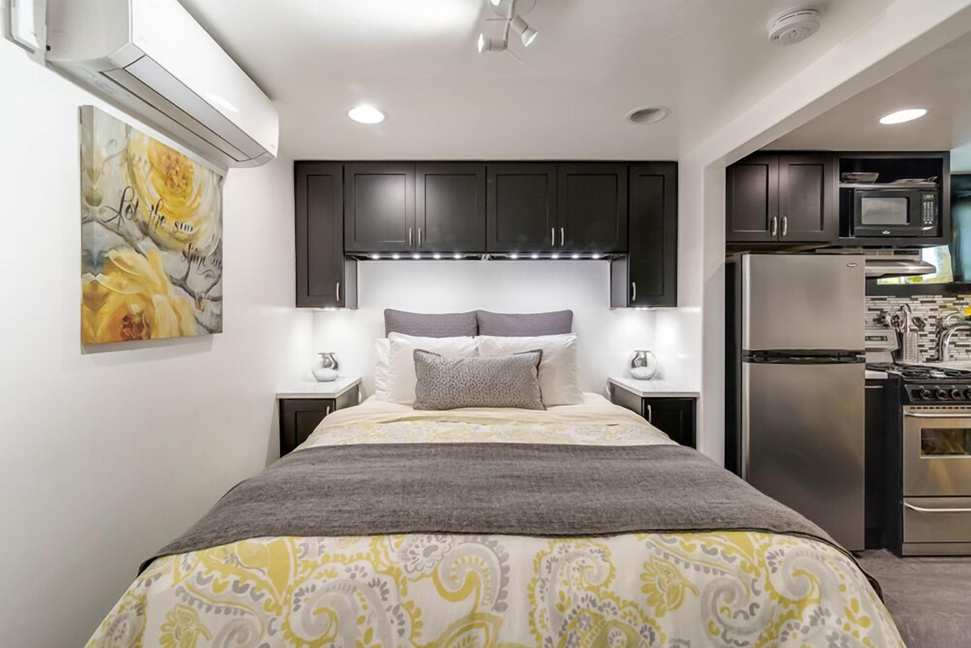 Un dormitorio con cama, mesitas de noche, cabecera y aire acondicionado instalado en la pared.