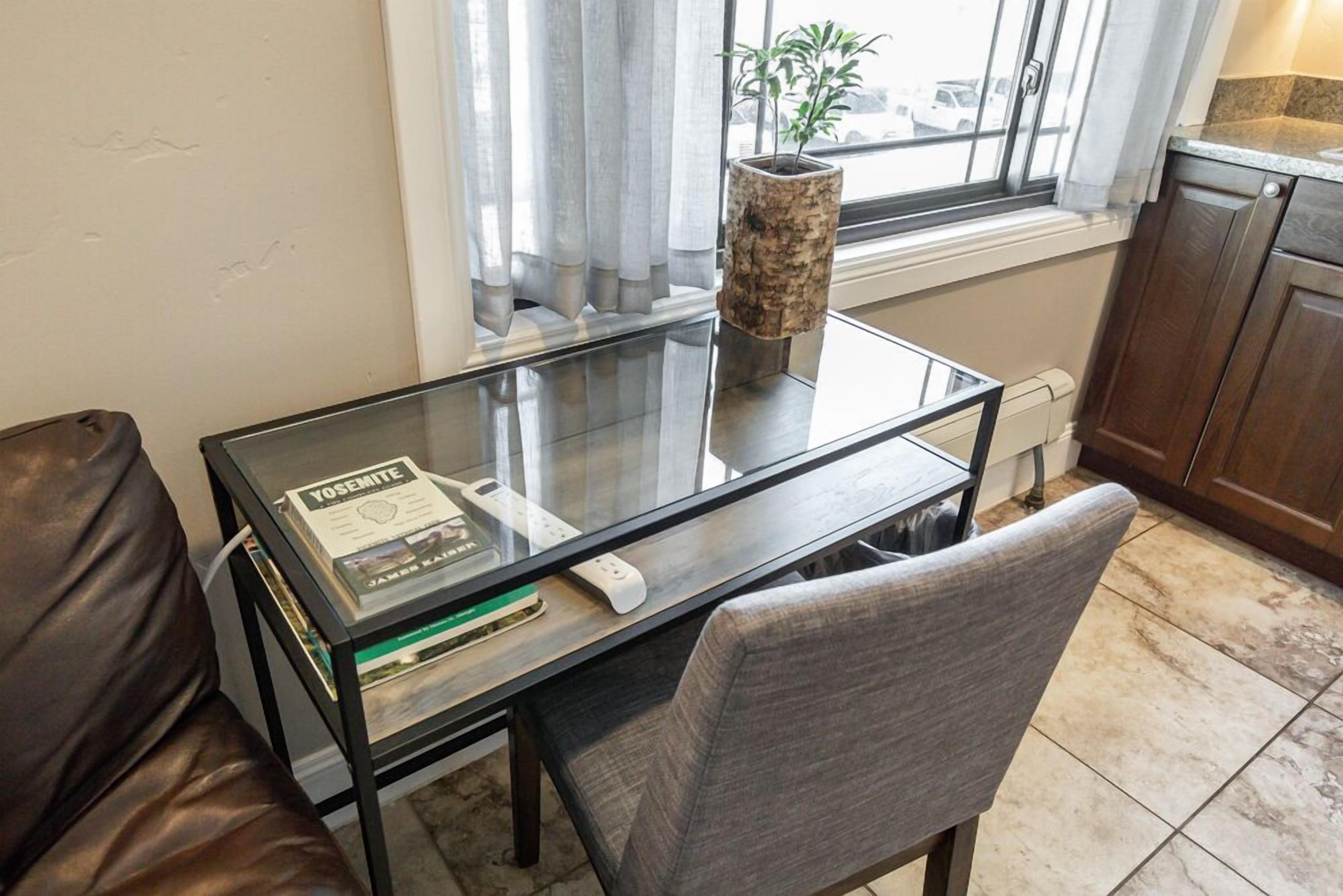 A modern kitchen with a glass-top dining table, a book titled "Yosemite," a potted plant, and wooden cabinets.