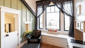 A compact kitchen with a stove, a window with curtains, a chair, and a small table. - Aspenwood Manor South (Provo)