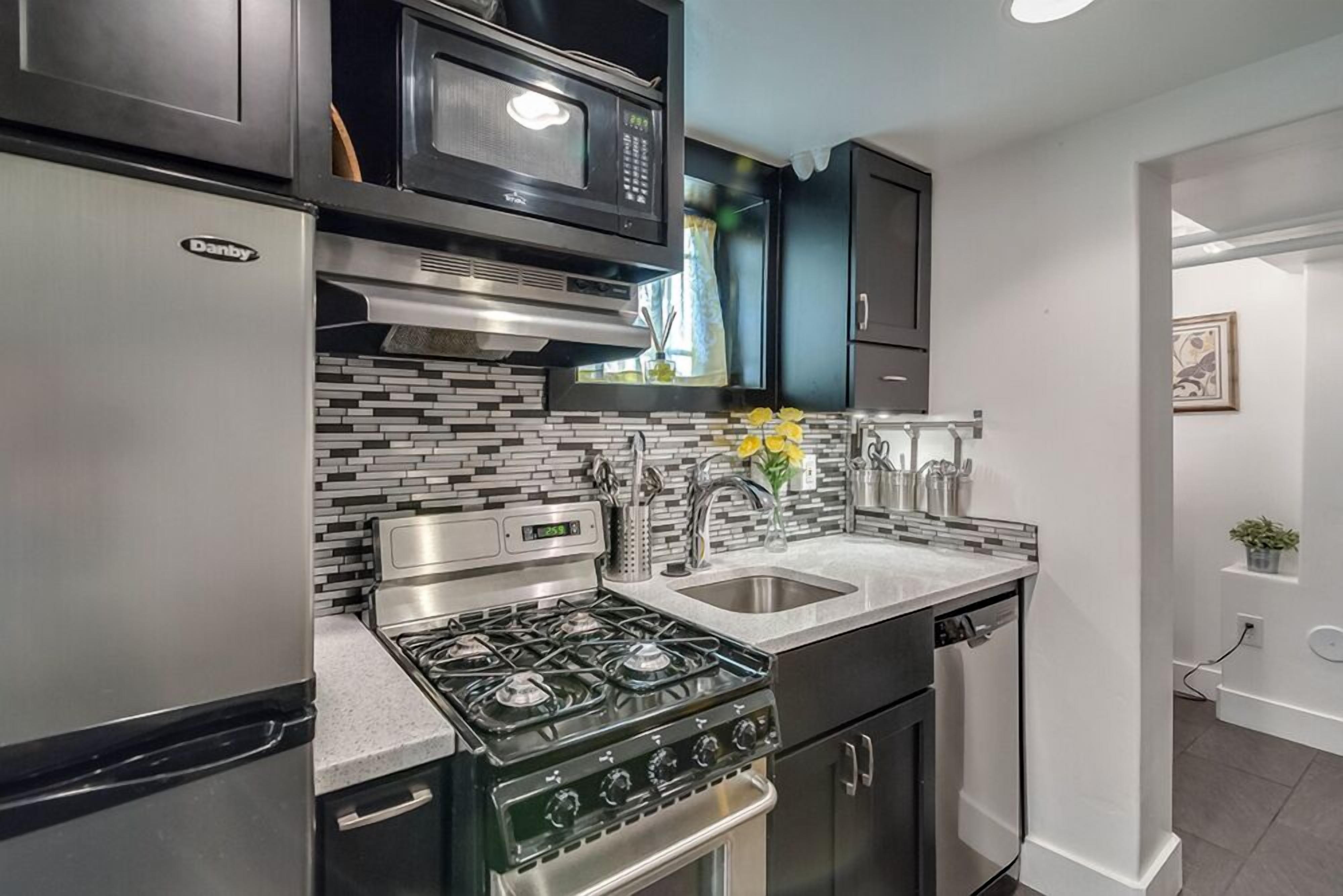 A modern kitchen with a Danby refrigerator, a black microwave, a gas stove, and a stainless steel sink.