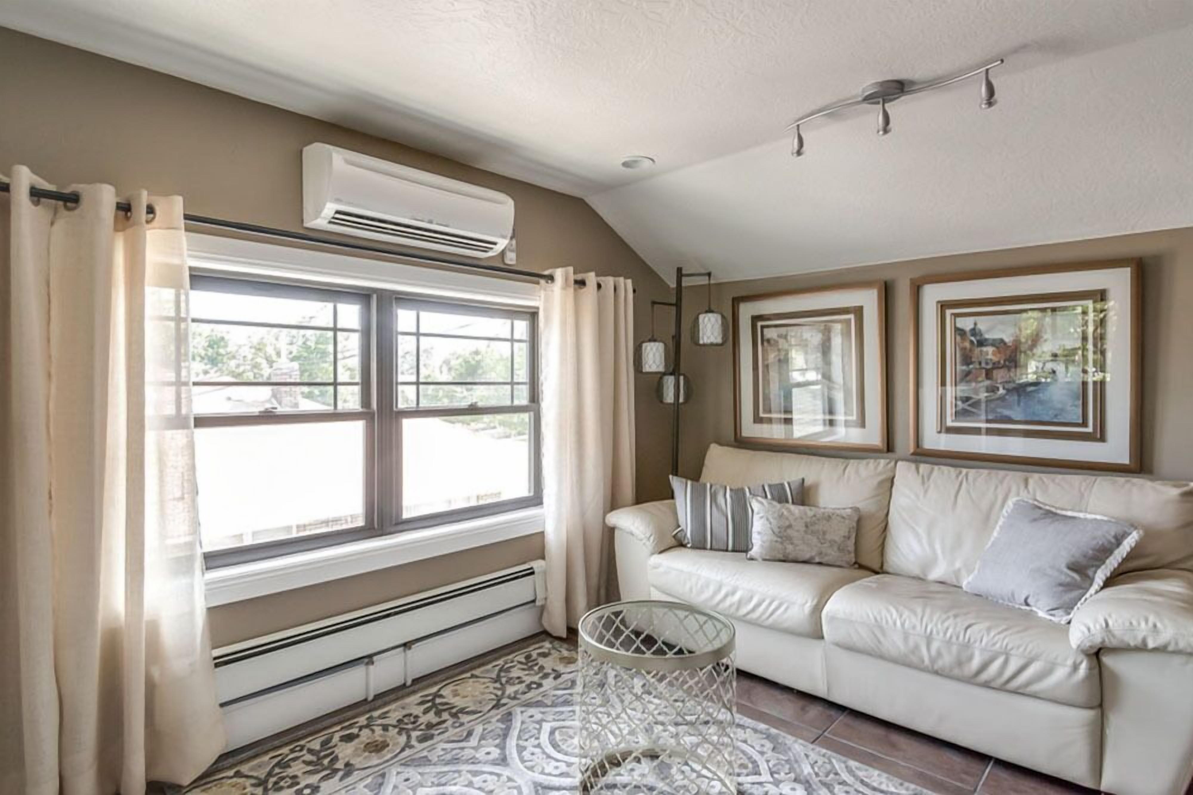 A living room with a beige sofa, a patterned rug, and framed pictures on the wall.