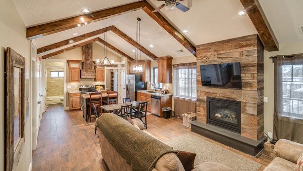 A spacious living area with a fireplace, wooden beams, and a television mounted on the wall. - Aspenwood Manor South (Provo)